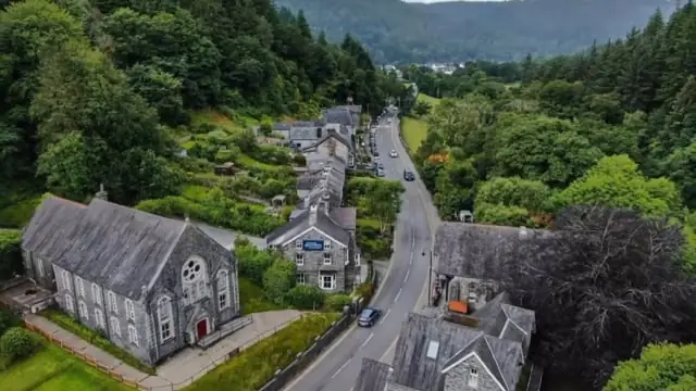 Aerial view of Betws-y-Coed: a slate-roofed village along a river road, wrapped in the forested hills of Eryri