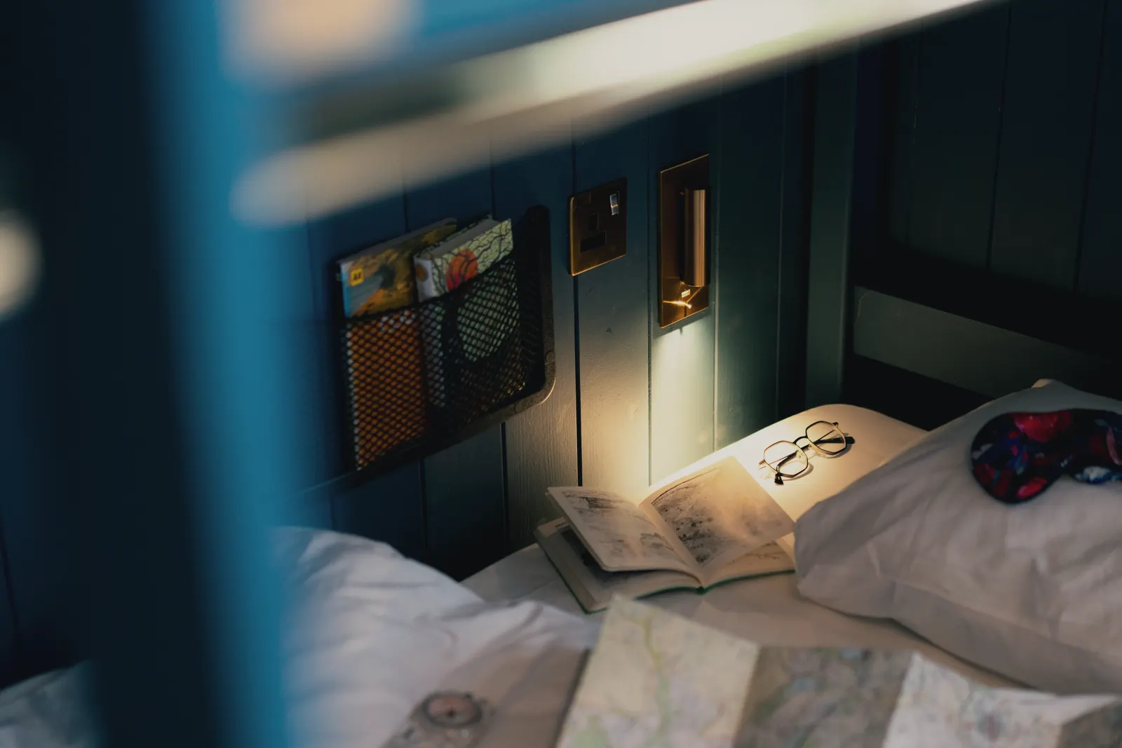 A made-up bunk with its own reading light in a dark-panelled dorm at Base Camp Hathersage