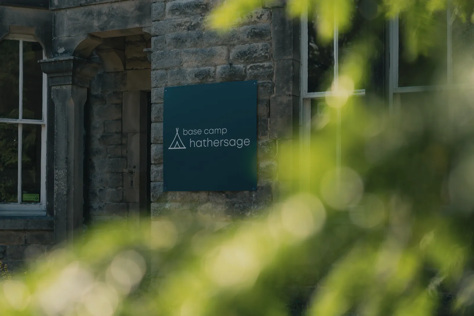 The Base Camp Hathersage sign by the front door, framed by greenery
