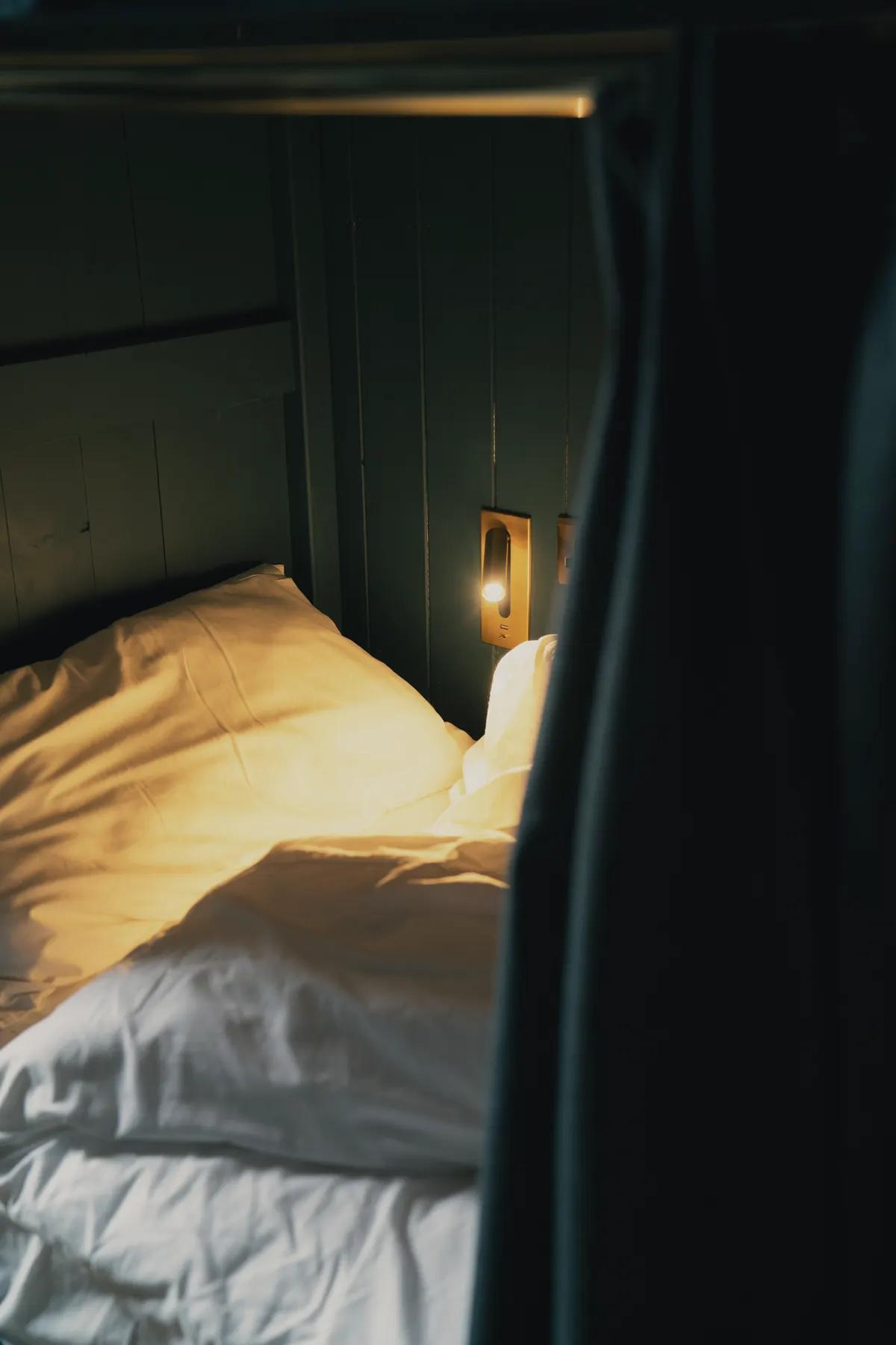 A bunk at Base Camp Hathersage with a mustard pillow, white linen and its own reading light