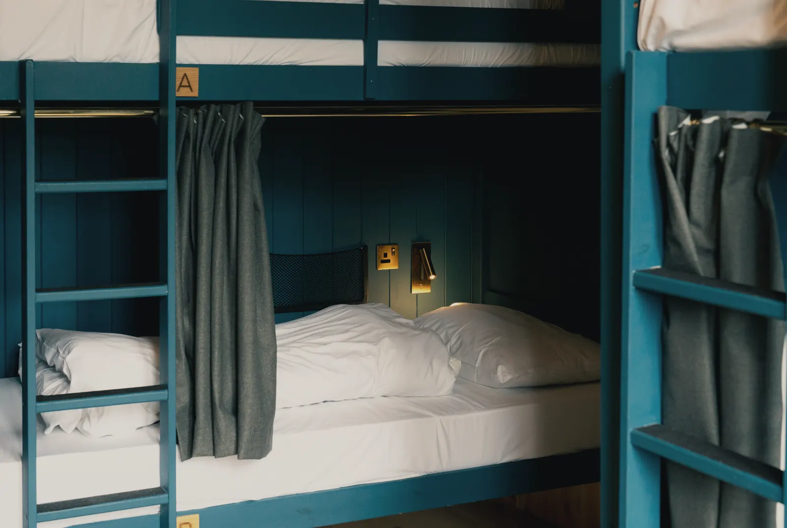 A row of dark-blue timber bunks made up with crisp white linen at Base Camp Hathersage