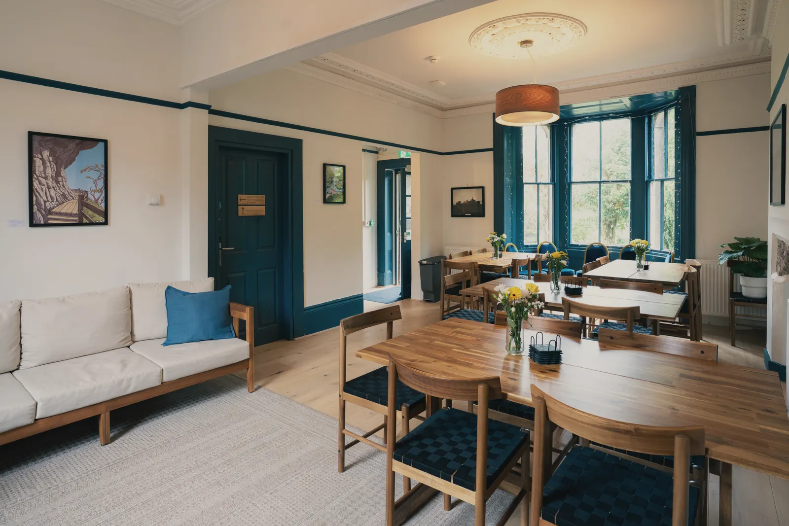 The long shared dining table in the blue-panelled kitchen, sun coming through the sash windows