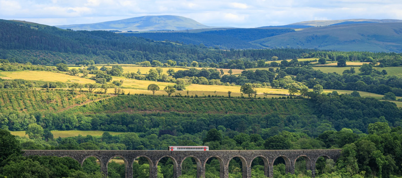 A train crossing a viaduct through the green hills of Wales